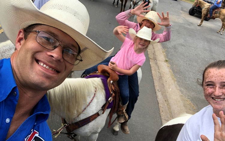 Un vaquero haciéndose una foto con dos chicas sobre un pony y otra chica sonriendo.